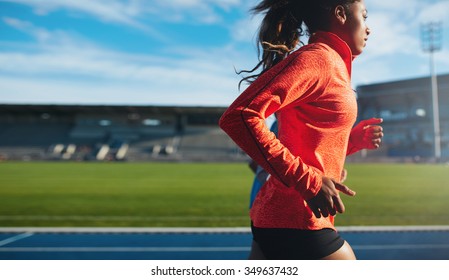Side view of fit young woman running. African female athlete training on race track at athletics stadium.