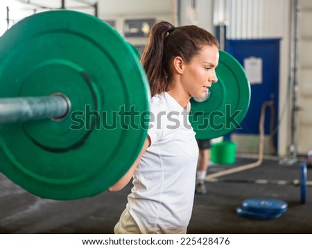 Side view of fit young woman lifting barbell in cross training box