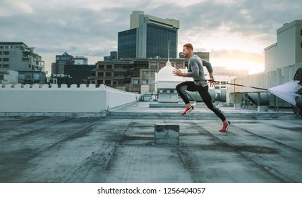 Side view of a fitness man running on rooftop using resistance parachute. Athlete training on rooftop running with a parachute tied to his waist.