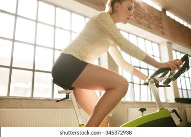 Side view of fitness woman on bicycle in gym. Young female athlete on bicycles at health club.