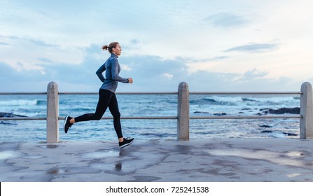 Side View Of Fitness Woman Running On A Road By The Sea. Sportswoman Training On Seaside Promenade.