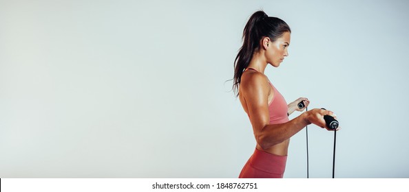 Side view of a fitness woman standing with a skipping rope. Woman in fitness wear training with a skipping rope. - Powered by Shutterstock