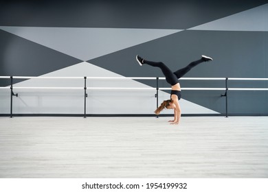 Side View Of Flexible Adult Female Dancer Training In Dance Hall, Handrails On Background. Strong Fit Woman Practicing Wheel In Jump, Doing Split In Air. Concept Of Choreography, Healthy Lifestyle.