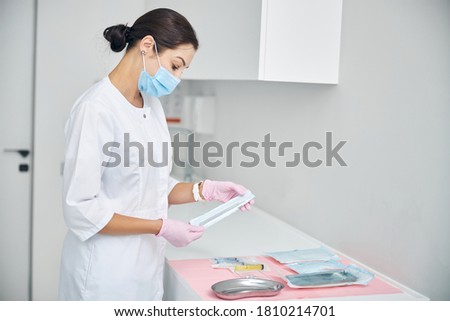 Side view of a focused female dermatologist staring at a set of sealed medical instruments