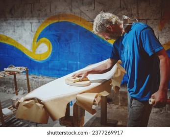 Side view of focused male shaper smoothing surface of surfboard with abrasive instrument in workshop - Powered by Shutterstock