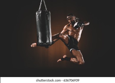 side view of focused muay thai fighter practicing kick on punching bag, action sport concept - Powered by Shutterstock