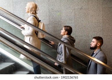 Side View Of Focused People Coming Out Of  Walkway, Moving Up On Escalator..