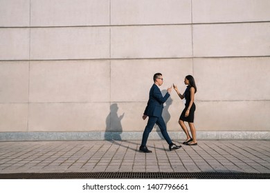 Side view of formal woman and man passing each other and using smartphone being inattentive while walking down street in sunlight - Shutterstock ID 1407796661