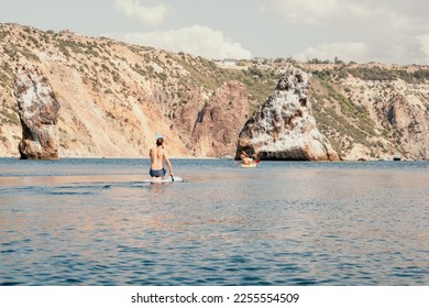 Side view foto of a man swiming and relaxing on the sup board. Sportive man in the sea on the Stand Up Paddle Board SUP. The concept of an active and healthy life in harmony with nature. - Shutterstock ID 2255554509