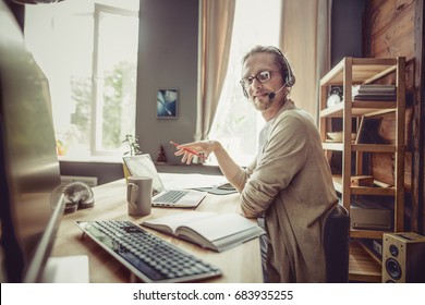 Side view of freelancer using headphones and microphone. Young man working from home.
