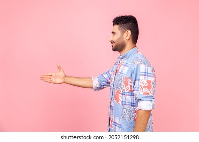 Side View Of Friendly Bearded Man In Casual Style Blue Shirt Reaching Out Hand To Handshake, Getting Acquainted At Job Interview, Meeting New People. Indoor Studio Shot Isolated On Pink Background.