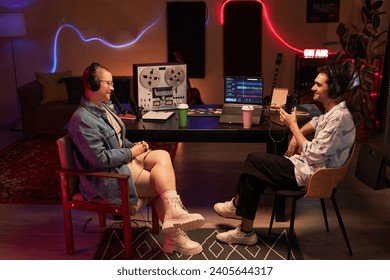 Side view of friendly young girl and cheerful adult man recording podcast while sitting in cozy studio with neon light - Powered by Shutterstock