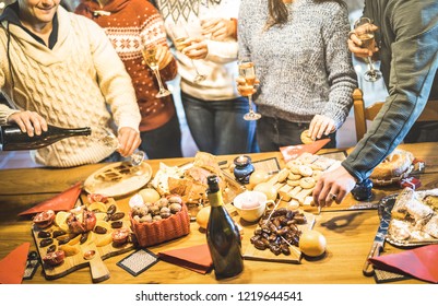 Side view of friends group tasting christmas sweets food and having fun at home drinking champagne sparkling wine - Winter holidays concept with people enjoying time eating together - Warm filter