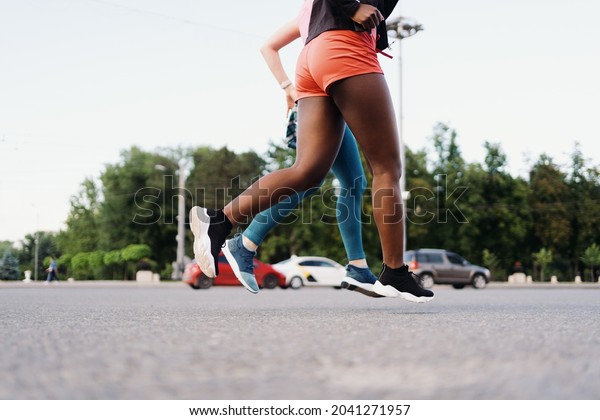 Side view of friends legs\
in sportswear running in the city. Multiethnic women having a\
fitness workout.