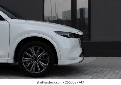 Side view of the front of a white SUV parked close to a building with cityscape reflection in window 