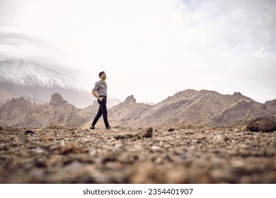 Side view full body ground level of bearded Hispanic male traveler walking with hands in pockets on rocky terrain near mountain Teide and looking away in Tenerife Canary Islands Spain - Powered by Shutterstock