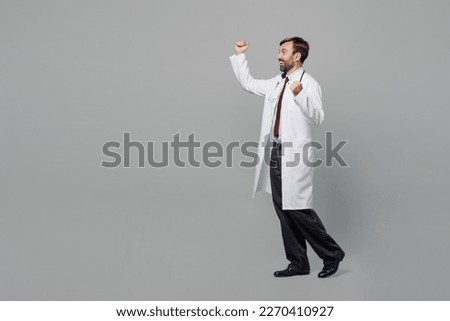Side view full body happy fun male doctor man wears white medical gown suit work in hospital doing winner gesture isolated on plain grey color background studio portrait. Healthcare medicine concept