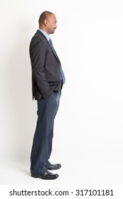 Side View Full Body Mature Indian Business Man Looking Forward, Standing On Plain Background.