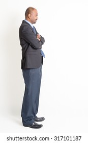 Side View Full Body Mature Indian Business Man Arms Crossed, Standing On Plain Background.