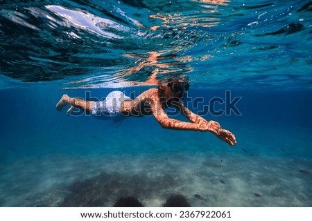 Side view full body of preteen kid in snorkeling mask and tube swimming under transparent seawater during vacation while exploring bottom