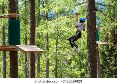 Side view full body of teenager in protective helmet riding on rope while entertaining in green jungle park
