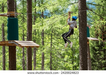 Side view full body of teenager in protective helmet riding on rope while entertaining in green jungle park