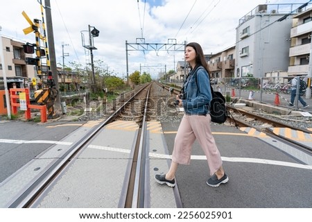 side view with full length asian Japanese female traveler walking across railway crossing in uji city Kyoto japan on a sunny day in spring