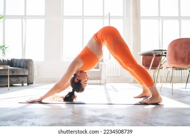 Side view full length of flexible female in sportswear performing Downward Facing Dog pose while doing yoga on mat in spacious studio