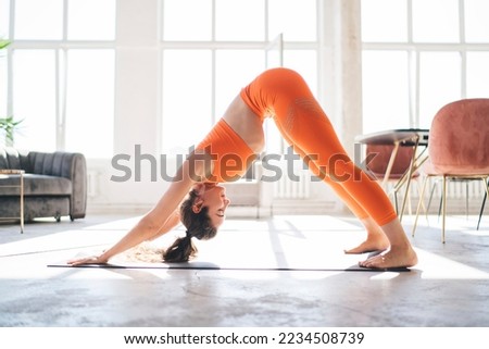 Side view full length of flexible female in sportswear performing Downward Facing Dog pose while doing yoga on mat in spacious studio