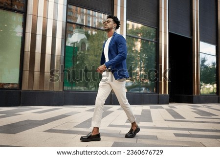 Side view full length man walks outside and wears trendy business clothes, blue jacket, white pants and loafer shoes. Stylish fashion male model, Street style.