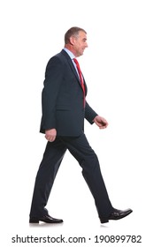 Side View Full Length Photo Of A Mid Aged Business Man Walking Forward And Looking Away. Isolated On A White Background