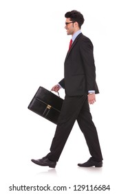 Side View Full Length Picture Of A Young Business Man Walking Forward With A Briefcase In One Of His Hands And Looking Away From The Camera On White Background