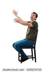 Side View Full Length Portrait Of Excited Casual Young Man Seated On A Chair Keeps Arms Outstretched For Hug Like Greeting An Old Friend Isolated Over White Background With Copy Space.