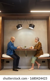 Side View Full Length Portrait Of Two People Sitting At Table In Indoor Cafe During Business Meeting, Copy Space