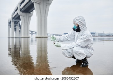 Side view full length portrait of scientist wearing hazmat suit collecting water samples, hands holding test tube, copy space - Powered by Shutterstock