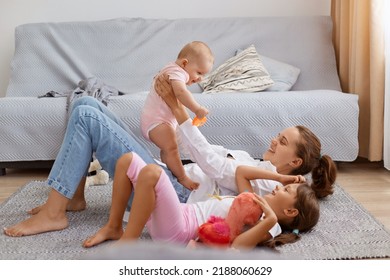 Side View Full Length Portrait Of Smiling Woman Holding Baby Daughter In Hands While Lying On Floor, Mother Playing With Her Children, Enjoying To Spend Time Together.