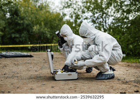 Side view full length of two people working on crime scene and using equipment case while wearing protective suits, copy space