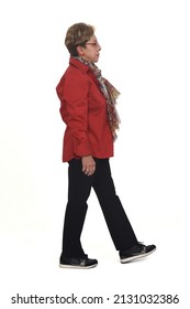 Side View Of A Full Portrait Of Senior Woman With Shirt And Pants, Serios  Looking At Camera And Walking On White Background