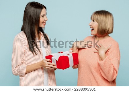Side view fun amazed elder parent mom with young adult daughter two women together wear casual clothes hold present box with gift ribbon bow isolated on plain blue cyan background. Family day concept