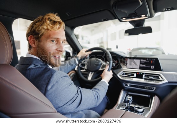 Side view fun businessman blond man driver male\
cabdriver in classic grey suit driving car hold wheel in traffic\
jam look camera testing auto want buy new automobile vehicle Sale\
transport concept.