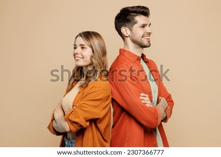 Side view fun young couple two friends family man woman wear casual clothes stand back to back hold hands crossed folded together isolated on pastel plain light beige color background studio portrait