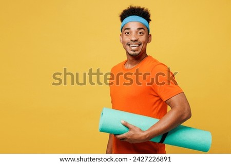 Side view fun young fitness trainer instructor sporty man sportsman wear orange t-shirt hold in hand yoga mat spend time in home gym isolated on plain yellow background. Workout sport fit abs concept