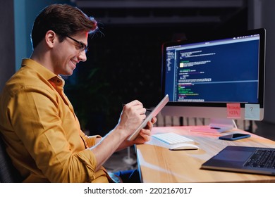 Side view fun young software engineer IT specialist programmer man in shirt work at home writing code on desktop pc computer, using tablet for surfing browsing internet. Program development concept - Shutterstock ID 2202167017