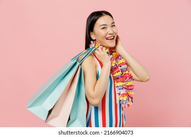 Side view fun young woman of Asian ethnicity in striped swimsuit hawaii lei hold package bags with purchases after shopping isolated on plain pastel pink background. Summer vacation sea rest concept