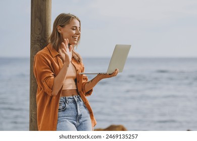 Side view fun young IT woman she wears orange shirt casual clothes hold use work on laptop pc computer waving hand walk on sea ocean sand shore beach outdoor seaside in summer day. Lifestyle concept - Powered by Shutterstock