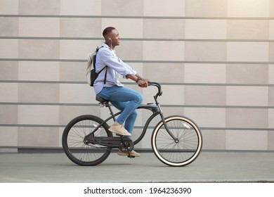 Side view of funky black guy with earphones racing on his bicycle near brick wall downtown - Powered by Shutterstock