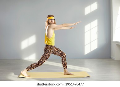 Side view of funny skinny young nerd guy in yellow sweatband and hilarious leopard leggings doing forward lunges and looking at camera standing on sports mat during fitness workout at gym or at home