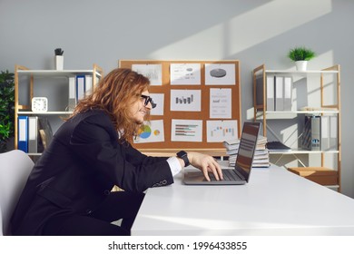 Side view of a funny strange male office worker working on laptop sitting at desk in office. Office worker or accountant with long uncombed hair makes financial reports or checks electronic documents. - Powered by Shutterstock