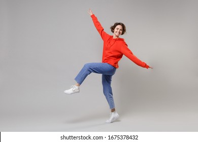 Side view of funny young brunette woman girl in casual red hoodie blue jeans posing isolated on grey wall background. People lifestyle concept. Mock up copy space. Dancing, spreading hands and legs - Shutterstock ID 1675378432