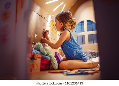 Side view of girl drawing with crayon on wall of carton house sitting inside and having fun at home.